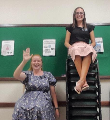 Alyssa waves while Sister Leopoldes sits on a tall stack of chairs